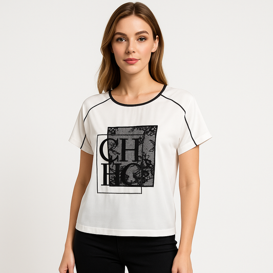 Moteris dėvi baltą palaidinę trumpomis rankovėmis, dekoruotą juodais akcentais ir elegantiška nėrinių aplikacija priekyje – laisvo kirpimo, derinama su kasdieniu arba pusiau formaliu įvaizdžiu.