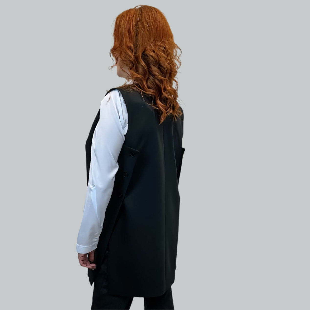 Moteris dėvi ilgą juodą klasikine liemenę su subtiliomis detalėmis – priekyje