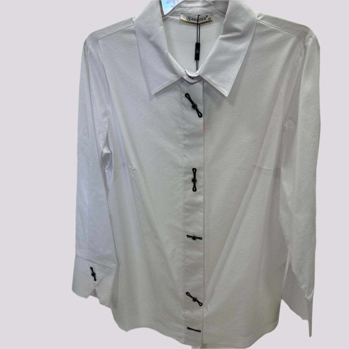 Klasikiniai balti moteriški marškiniai su dekoruotomis sagomis, pakabinti ant pakabos – priekis.