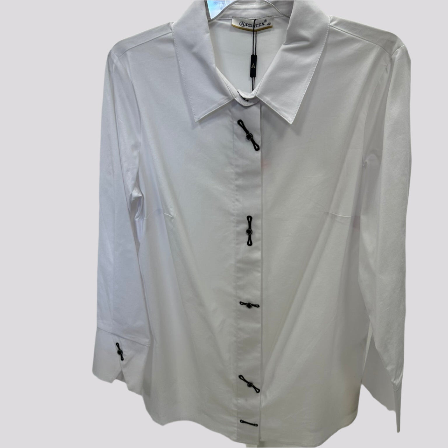 Klasikiniai balti moteriški marškiniai su dekoruotomis sagomis, pakabinti ant pakabos – priekis.