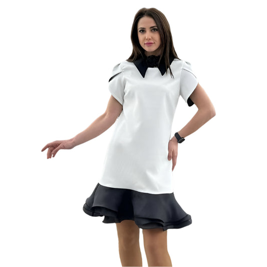 Moteris dėvi trumpą baltą suknelę su juodu atlapu ir dekoratyviniu sijonu, tinka įvairioms šventėms