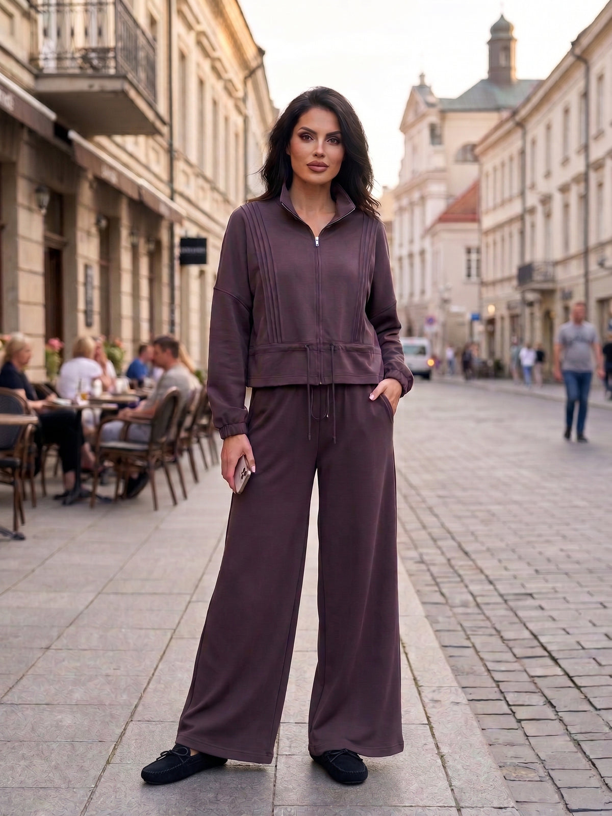 Moteris vilki elegantišką šokolado spalvos kostiumėlį su plačiomis palazzo kelnėmis