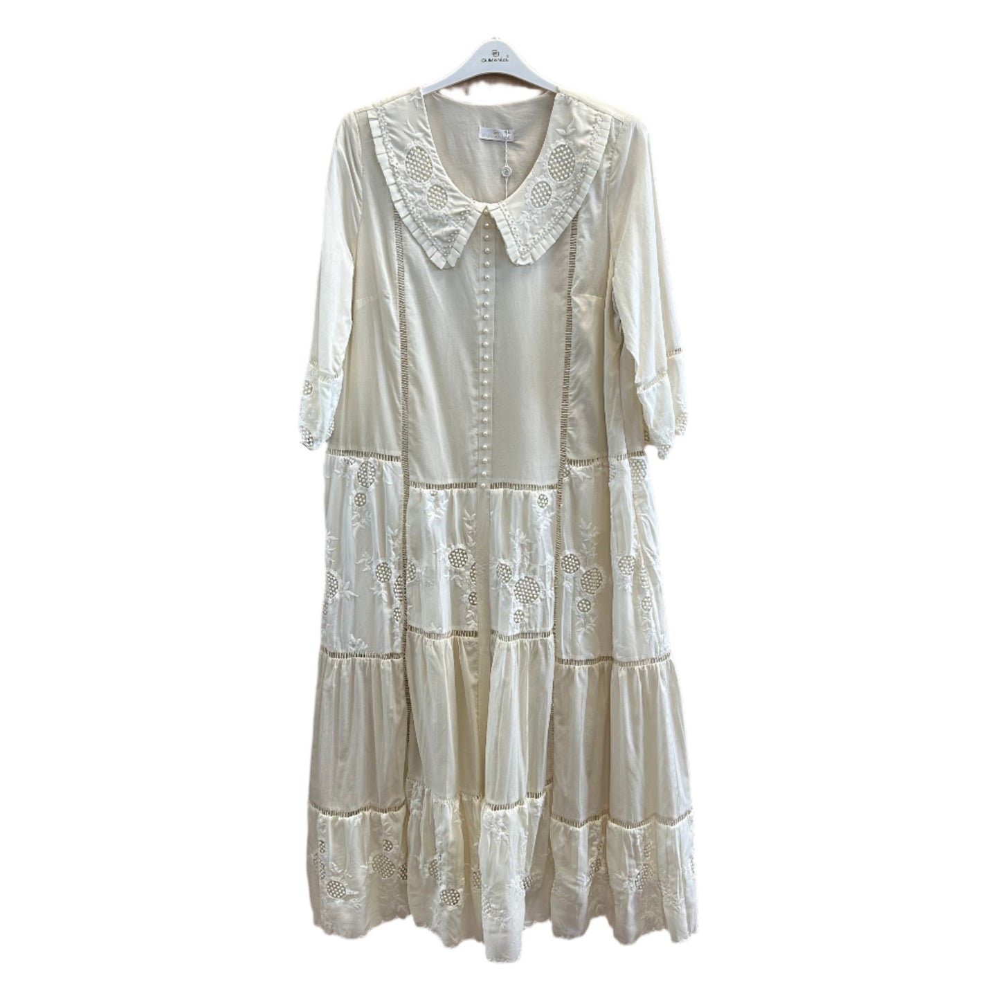 Ilga bohemiško stiliaus suknelė su nėriniuota apykakle ir perliukų sagomis, dekoruota siuvinėtais intarpais, pakabinta ant pakabos.