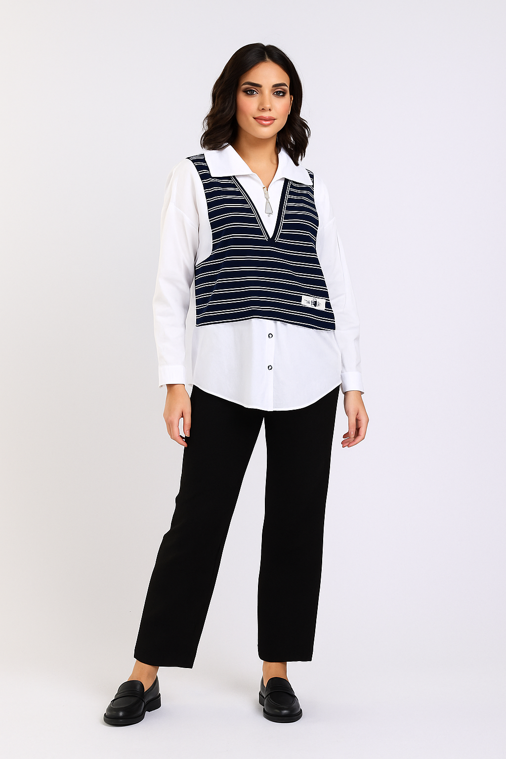 Woman wearing a white blouse with a black and white striped vest and black pants on a white background
