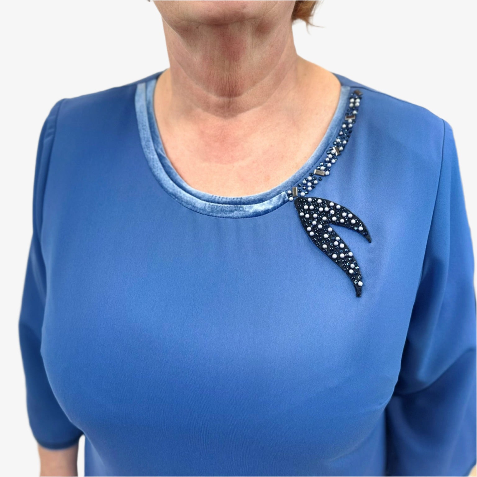 Artimas žvilgsnis į žydros suknelės blizgantį kaklo papuošimą.