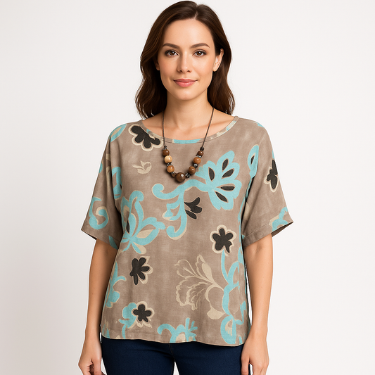 Moteris dėvi palaidinę su kūno spalvos pagrindu ir mėtų žalumo raštais – lengvas ir stilingas derinys.