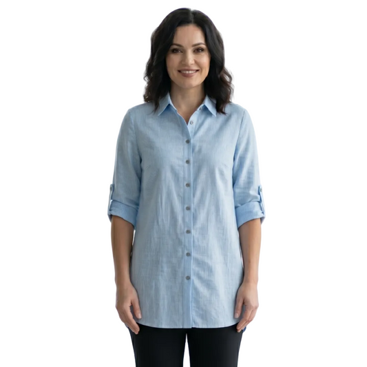 Woman wearing a light blue shirt and black pants standing in a bright room with large windows.