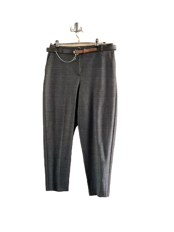 A pair of gray plaid cropped trousers hanging on a wooden door in a clothing store, with racks of other garments visible in the background and foreground.