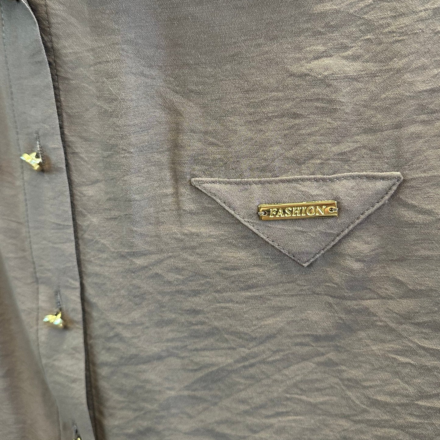 Dekoratyvinė trikampė kišenė su aukso spalvos „FASHION“ užrašu ant šokolado spalvos palaidinės.

